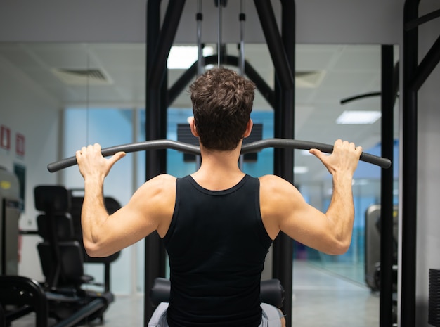 Mann, der eine Lat-Maschine in einem Fitnessstudio benutzt, um seine Schultern und seinen Rücken zu trainieren