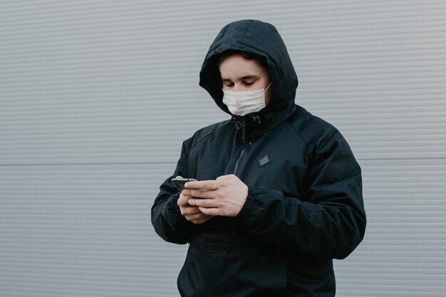 Mann, der eine Maske mit Smartphone auf einem neutralen Hintergrund trägt.