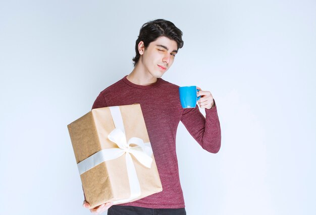 Mann, der eine Pappgeschenkbox hält und eine Tasse Tee hat.