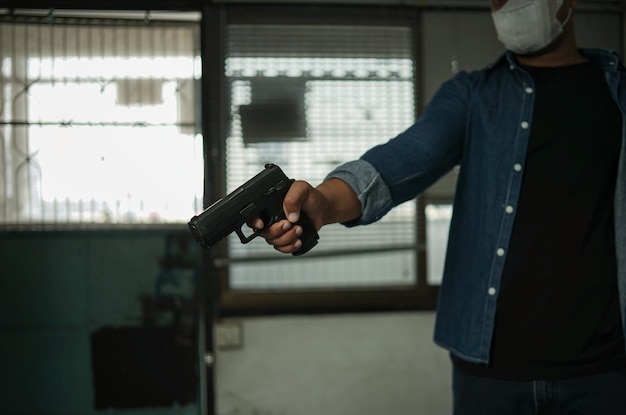 Mann, der eine Pistole hält, die in einem Raum in Schwarz stehtKonzept des Mordverbrechers