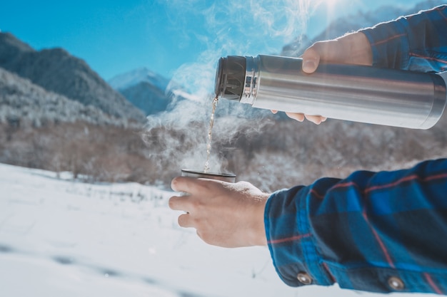 Mann, der eine Thermoskanne auf einem schneebedeckten Berg hält