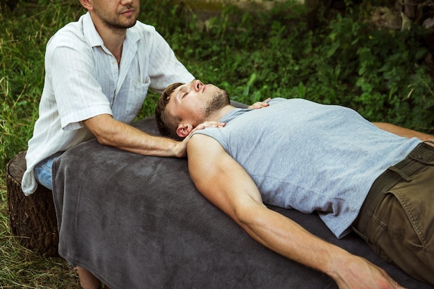 Mann, der einem Mann in der Natur eine osteopathische Kopfmassage gibt 2