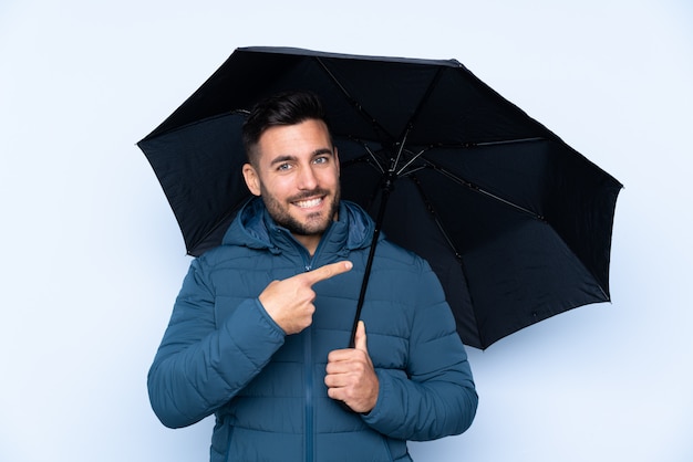 Mann, der einen Regenschirm über isolierte Wand hält und darauf zeigt