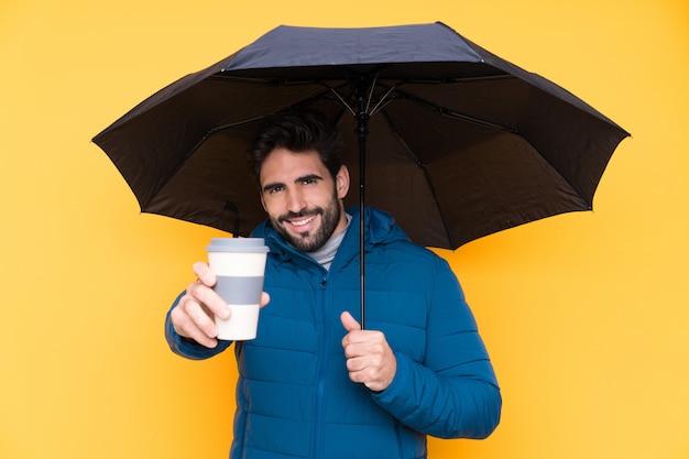 Mann, der einen Regenschirm über lokalisierter gelber Wand hält