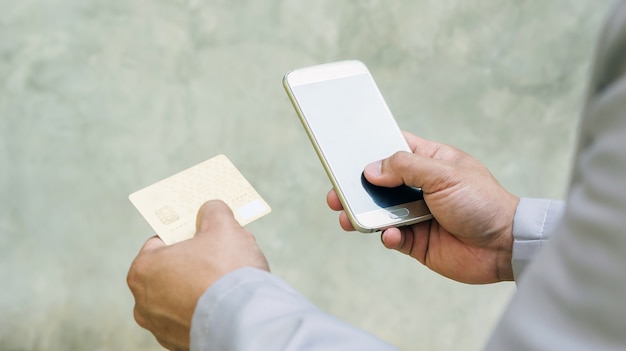 Mann, der einen Smartphone und eine Kreditkarte auf einem grauen Hintergrund verwendet.