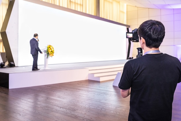 Foto mann, der einen sprecher mit weißem wandbildschirm für präsentation aufzeichnet