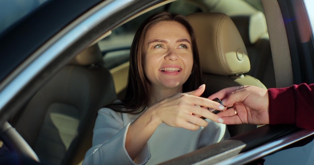 Mann, der einer jungen Frau Schlüssel gibt, die im Auto sitzt. Frohe geschäftsführende Frau, die Schlüssel vom neuen Auto erhält. Glücklicher Autobesitzer, der Transport im modernen Salon kauft.