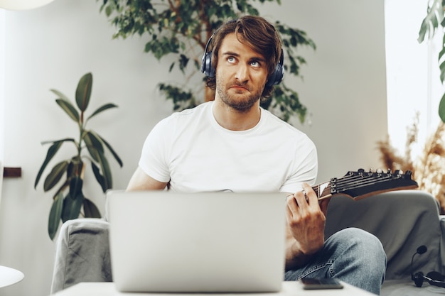 Mann, der elektrische Gitarre spielt und Musik in Laptop aufzeichnet