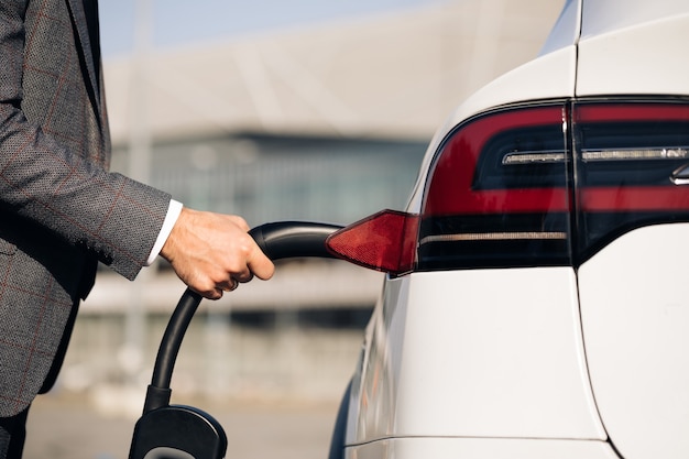 Mann, der Elektroauto an der elektronischen Autoladestation einsteckt