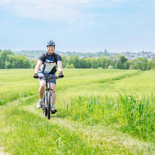 Mann, der Fahrrad auf dem Weg im grünen Gerstenfeld-Kopienraum fährt