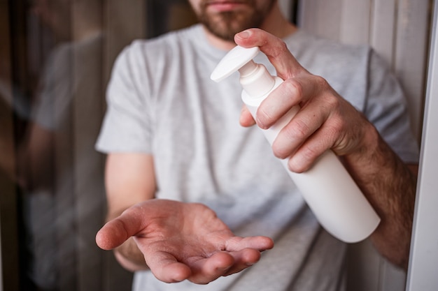 Mann, der Feuchtigkeitslotion aufträgt, die von der Flasche auf seine Hand mit sehr trockener Haut mit Creme wegen des Waschens von Alkohol fällt