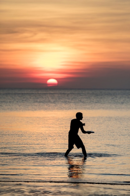 Mann, der fliegenden Teller auf Meer Beac gegen schönen Sonnenunterganghimmel am reisenden Bestimmungsort spielt