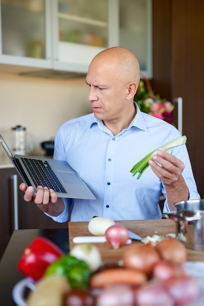 Mann, der Gemüsesalat vorbereitet, während auf Laptop schaut