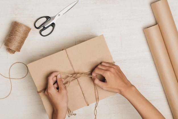 Mann, der Geschenk verpackt. Ein in braunes Papier gewickeltes und mit grober Schnur zusammengebundenes Paket