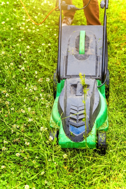 Mann, der grünes Gras mit Rasenmäher im Hinterhof schneidet. Hintergrund des Gartenlandeslebensstils.