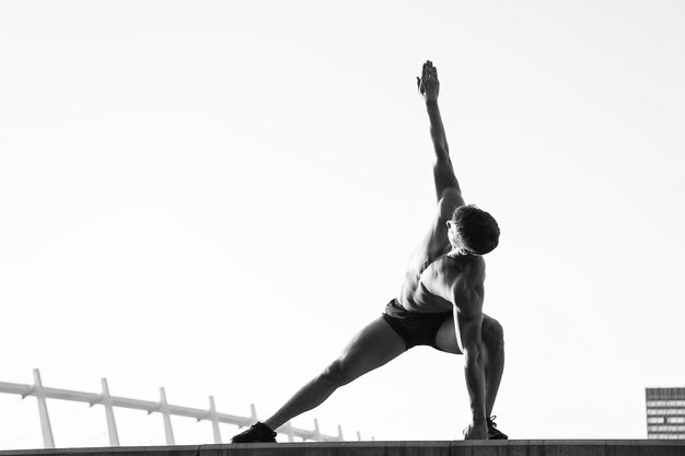 Mann, der Hände und Beine auf dem Dach ausdehnt Sportler, der im Freien trainiert Gesundes Lebensstilkonzept Fitness und Sport Sportler mit muskulösem Körper auf weißem Himmel kopieren Raum