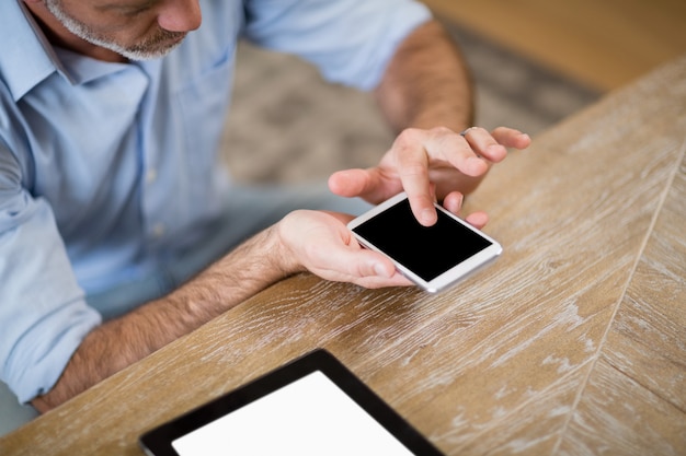 Mann, der Handy mit digitalem Tablett auf Tisch im Wohnzimmer verwendet