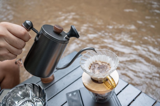 Mann, der heißen Kaffee tropft und in der Nähe des Flusses im Naturpark campiert. Outdoor-Aktivität und Entspannung im Urlaub.