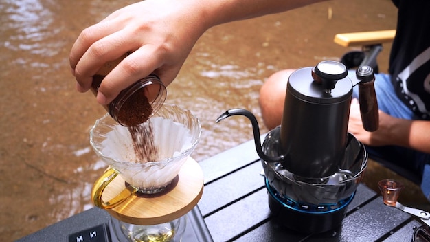 Mann, der heißen Kaffee tropft und in der Nähe des Flusses im Naturpark campiert. Outdoor-Aktivität und Entspannung im Urlaub.