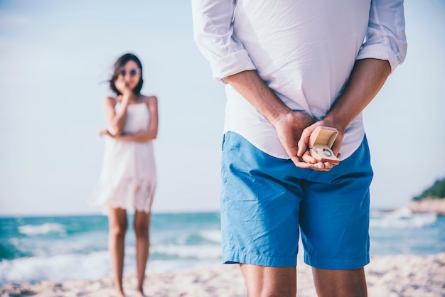 Mann, der hinter einen Ring versteckt, um seiner Freundin einen Überraschungsvorschlag am Strand zu machen.