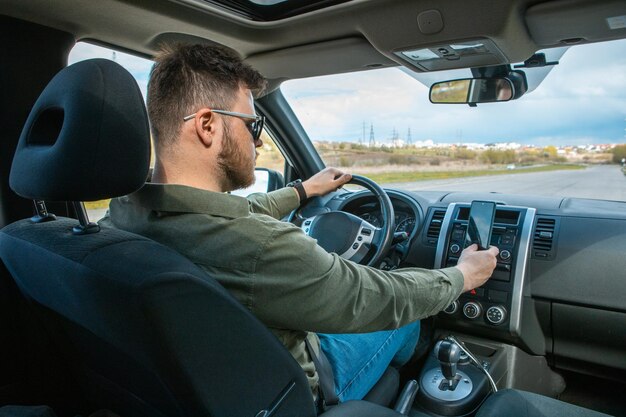 Mann, der im Auto mit Telefon sitzt, lenkt den Lebensstil ab