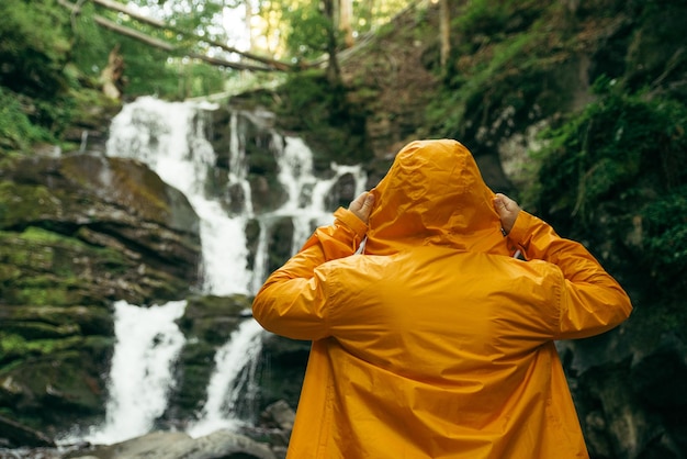 Mann, der im gelben Regenmantel steht und Wasserfall betrachtet