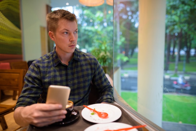 Mann, der im Kaffeehaus sitzt, während Handy benutzt und denkt