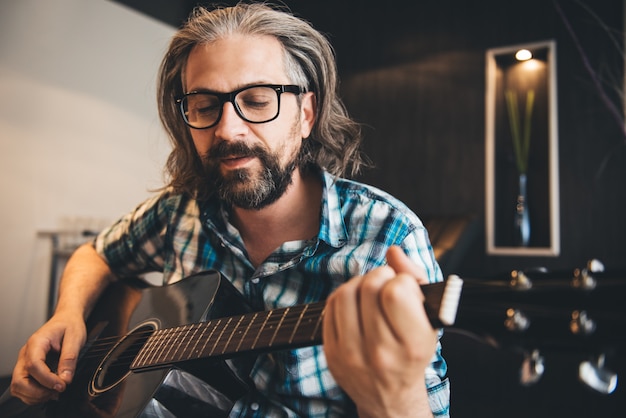 Mann, der im Sofa sitzt und zu Hause Gitarre spielt