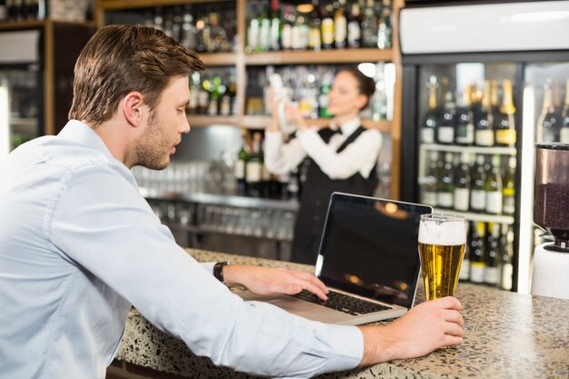 Mann, der in der Hand an Laptop mit Bier arbeitet