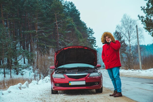 Foto mann, der in der nähe von kaputtem auto am straßenrand steht, schneit winterwetter. platz kopieren