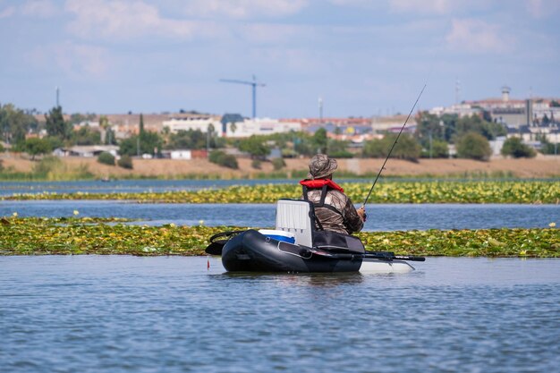 Mann, der in einem einzelnen Boot mitten im Fluss auf Karpfen fischt.