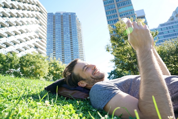 Mann, der in Park unter Verwendung des Smartphone legt