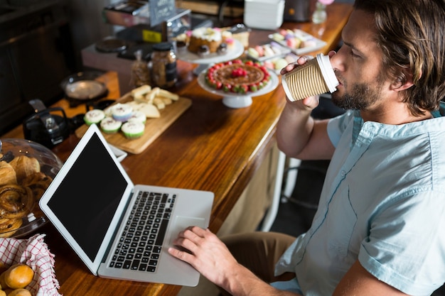 Mann, der Kaffee beim Verwenden des Laptops an der Theke hat