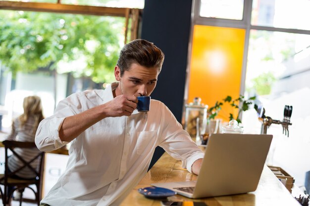 Mann, der Kaffee beim Verwenden des Laptops hat