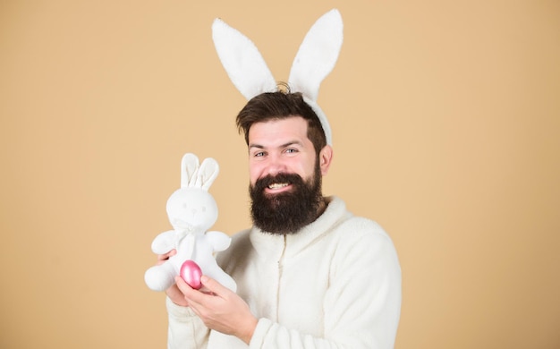 Mann, der Kaninchenanzug trägt, spielt mit Spielzeug. Weiche Ohren des lustigen Häschenmannes. Konzept für Osteraktivitäten. Immer noch kindisch. Feiern Sie Ostern. Kerl bärtiger Hipster fröhlicher Hase mit langen weißen Ohren. Osterhase.