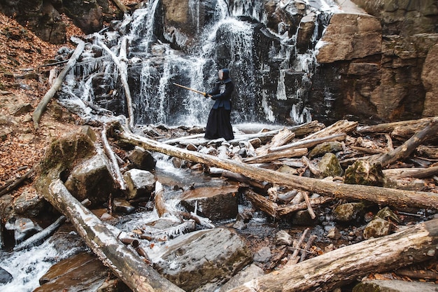 Mann, der Kendo mit Bambusschwert auf Wasserfallhintergrund übt