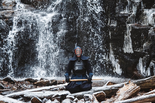 Mann, der Kendo mit Bambusschwert auf Wasserfallhintergrund übt