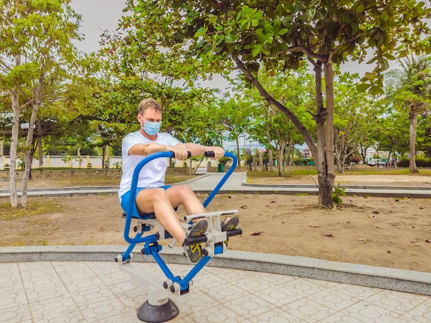 Mann, der körperliche Übungen macht, Liegestütze Kraftübungen lehnt sich in leeres Metall-Fitnessstudio im öffentlichen Stadtpark im Freien und trägt Maske allein zur Vorbeugung von Covid19 Gesunder Lebensstil in Quarantäne und Coronavirus