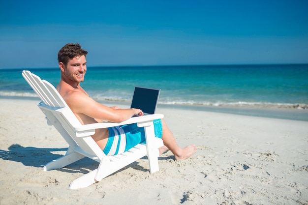 Mann, der Laptop auf Klappstuhl am Strand verwendet