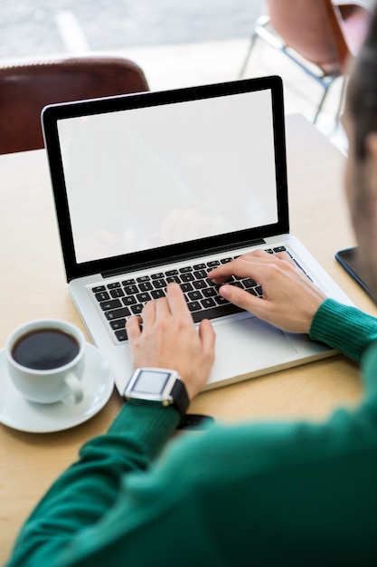 Mann, der Laptop mit Kaffeetasse auf Tisch verwendet