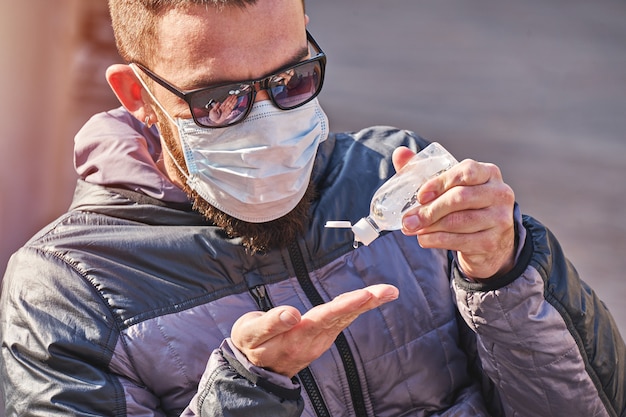 Mann, der Maske trägt, verwendet antibakterielles Gel auf Händen