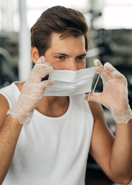 Foto mann, der medizinische maske an der turnhalle anzieht, während handschuhe tragen