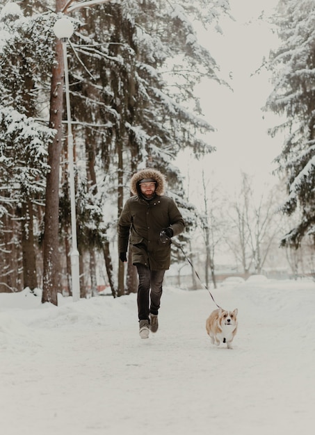 Mann, der mit Corgi-Hund im Winterpark spazieren geht