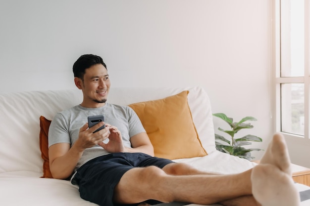 Mann, der mit der mobilen Anwendung zufrieden ist, während er sich auf seinem Sofa entspannt