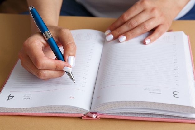 Mann, der mit einem blauen silbernen Metallstift in einem rosa Tagebuch schreibt