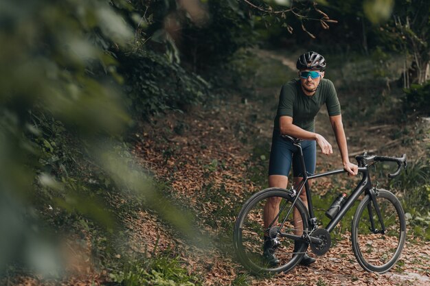 Mann, der mit Fahrrad im Park steht, während er sich nach dem Training ausruht