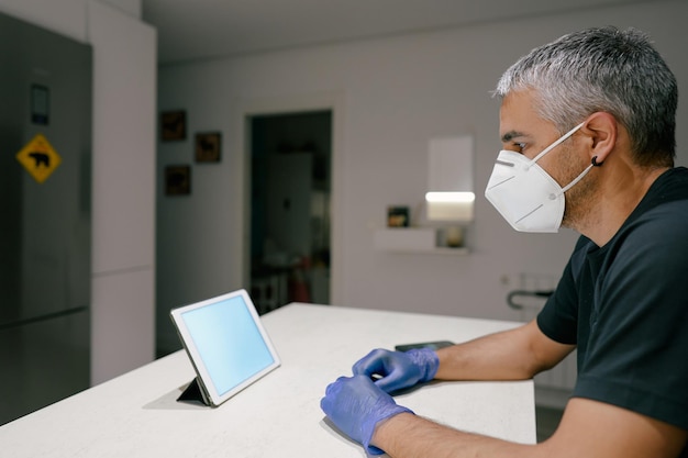 Foto mann, der mit handschuhen und maske auf ein tablet schaut covid19