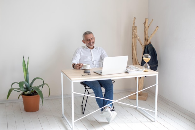 Mann, der mit Kaffee sitzt und auf den Laptop-Bildschirm lächelt