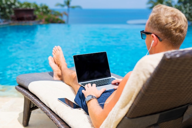Mann, der mit Laptop am Pool arbeitet