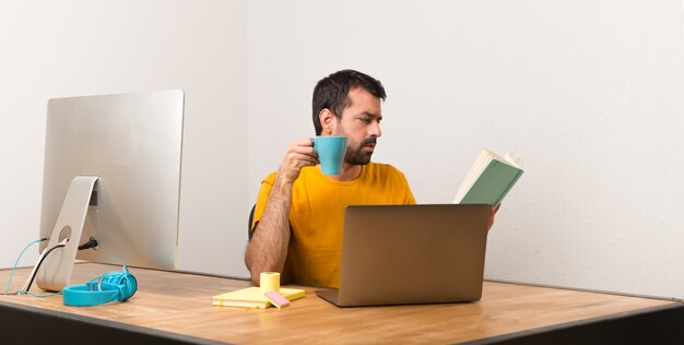 Mann, der mit laptot in einem Büro ein Buch lesend arbeitet